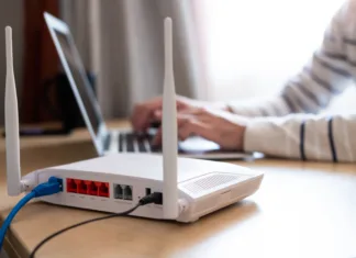 Kaj je WPS? Selective focus at router. Internet router on working table with blurred man connect the cable at the background. Fast and high speed internet connection from fiber line with LAN cable connection.