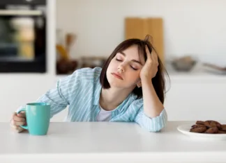 Zakaj si zjutraj tako zaspan in kakšne so posledice? Sleepy young woman drinking coffee, feeling tired, suffering from insomnia and sleeping disorder. Sad female sitting in modern kitchen interior, empty space
