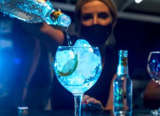 Recept za koktejl: Modra dama Young waitress with protective mask prepares a gin and tonic cocktail in a nightclub.