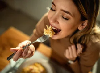 Intuitivno ali premišljeno prehranjevanje: Katero je boljše? Close-up of happy woman eating pasta for dinner.