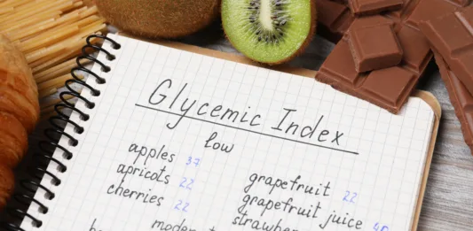 Notebook with products of low and moderate glycemic index, kiwi and chocolate on light wooden table, closeup