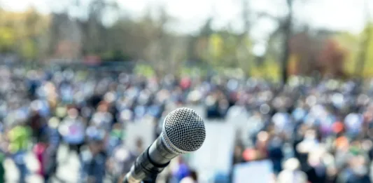 Protest or public demonstration, focus on microphone, blurred crowd of people in the background