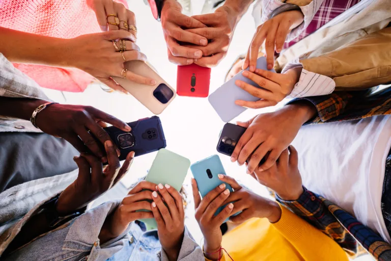 Young group of student people using smartphone together outside. Addicted millennial friends using cell phone at city street. Low angle view.