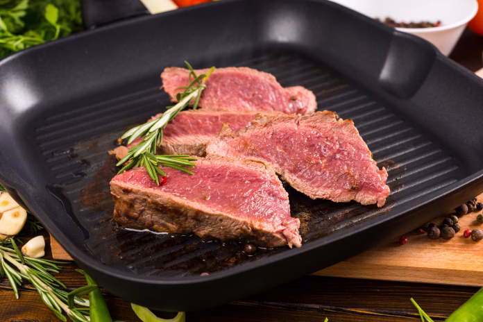 Close Up of Slices of Rare Roast Beef Frying on Ridged Skillet Cast Iron Pan and Seasoned with Fresh Herbs of Rosemary