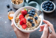 Kako pripraviti ovsene kosmiče na edini pravilen način Oatmeal porridge bowl with berry fruits in female hands, closeup view. Healthy vegetarian breakfast food