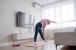 A woman is practicing yoga in a cozy living room on a pink mat, doing a warrior pose with a serene and focused look