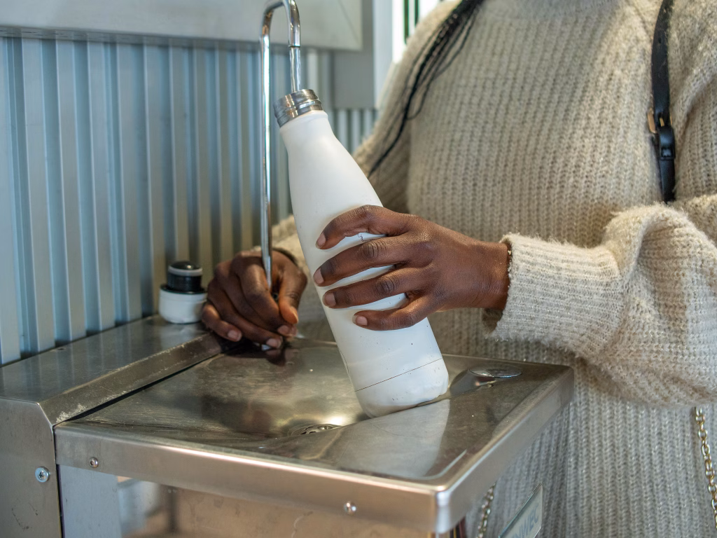 A young woman filling her reusable bottle at an airport fountain
