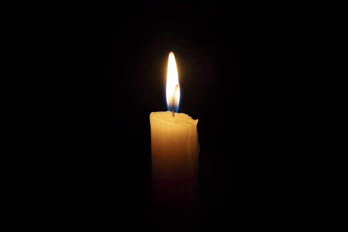 an orange candle burns in the dark on a black background. The concept of memory and sorrow.