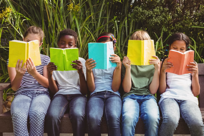 children-sitting-in-row-and-reading-books-at-the-park-stockpack-istock Children sitting in row and reading books at the park