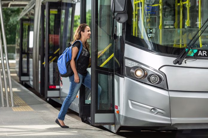 Sao Paulo, Brazil – February 13, 2016: A student with backpack on his back going to school, getting on a modern, gray bi-articulated municipal bus, stopped at the terminal