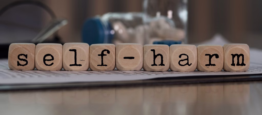 Word SELF-HARM composed of wooden dices. Pills, documents and a pen in the background. Closeup