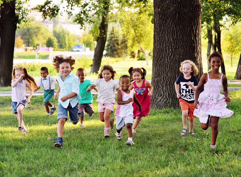 A group of happy children of boys and girls run in the Park on the grass on a Sunny summer day . The concept of ethnic friendship, peace, kindness, childhood.
