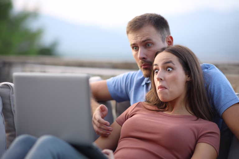 Confused couple watching media content on laptop sitting in a terrace at home