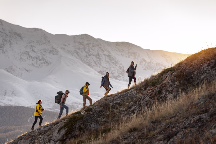group-of-young-active-hikers-with-backpacks-walks-uphill-in-mountains-at-sunset-stockpack-istock Group of young active hikers with backpacks walks uphill in mountains at sunset