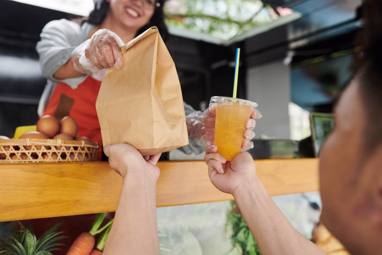 Man taking packed order and soft drink from hands of food truck worker