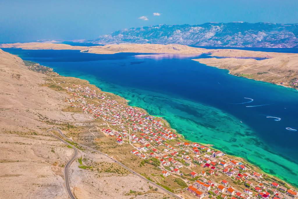 Scenic view of Pag unique rocky terrain and coastline, with the majestic Velebit Mountain range rising in the background, showcasing the striking contrast of sea and stone in northern Dalmatia