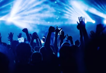 Najboljše pesmi Dan D Silhouettes of people rising their hands and dancing on an open air music festival. There are blue stage lights. People having fun at rock concert on a summer music festival.