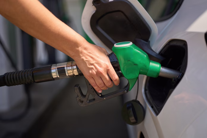 Close-up of a hand holding a green fuel pump nozzle, inserting it into a white car's tank