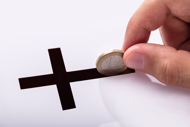 Close-up Of Hand Inserting Coin In Crucifix Slot On White Background