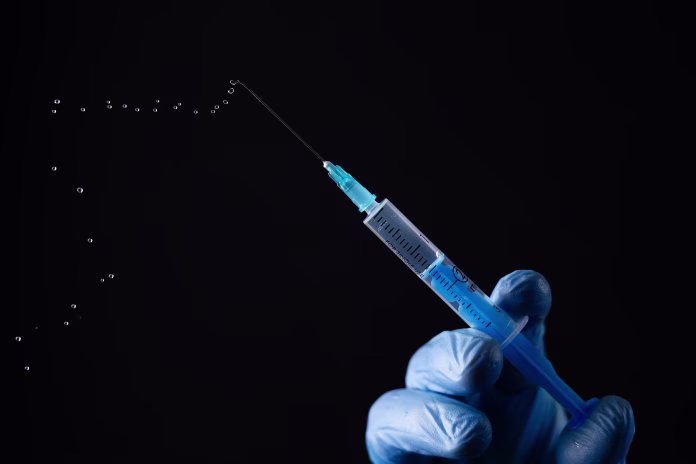 Doctors hand in surgical gloves holds a syringe on black background.