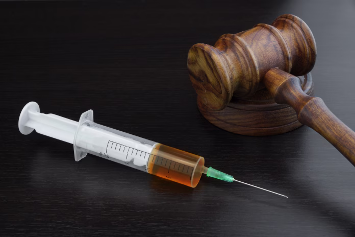 Judges Gavel And Medical Injection Syringe With Brown Liquid On The Black Wood Background, Close-up, Top View