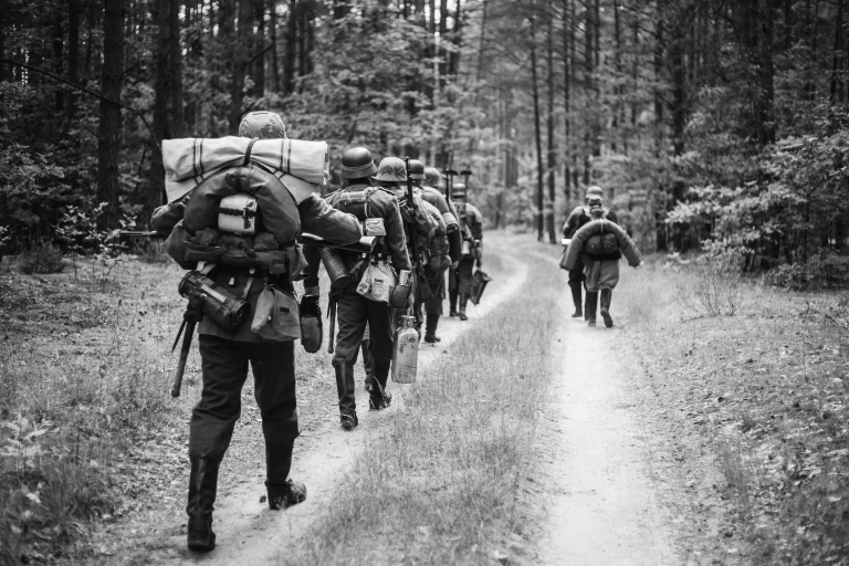 Re-enactors Dressed As German Infantry Soldiers In World War II Marching Walking Along Forest Road In Summer Day. Photo In Black And White Colors.