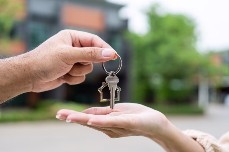 Woman buying or rent new home she holding key front of new house. Surprise happy young asian woman giving house key and smile to rent or purchase apartment home. Moving relocation concept.