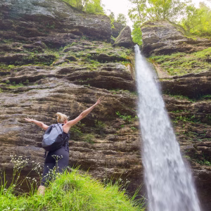 Female hiker raising arms inhaling fresh air, feeling relaxed and free in beautiful natural environment under Pericnik waterfall in Vrata Valley in Triglav National Park in Julian Alps, Slovenia.