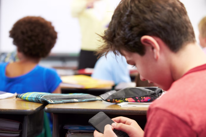 pupil-sending-text-message-on-mobile-phone-in-class-sitting-at-desk-stockpack-istock Pupil Sending Text Message On Mobile Phone In Class Sitting At Desk