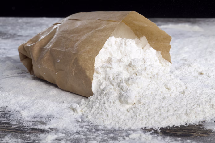 a small paper bag with durum wheat flour on the table, some of the flour powder spilled out of the bag
