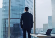 Elon Musk poražen, nič več ni prvi na lestvici najbogatejših Back View of the Thoughtful Businessman wearing a Suit Standing in His Office, Hands in Pockets and Contemplating Next Big Business Deal, Looking out of the Window. Big City Business District Panoramic Window View.