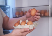 Ali moramo jajca hraniti v hladilniku? Close up of a man putting fresh eggs into refrigerator.