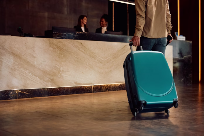 Close up of hotel guest with a suitcase arriving reception desk. Copy space.