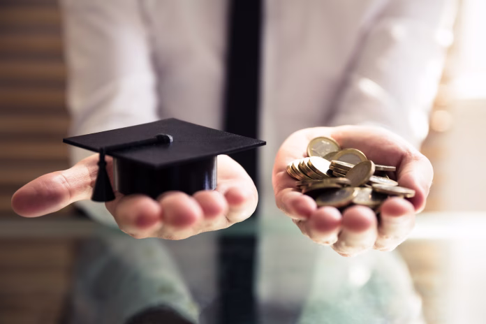 Human Hand Holding Black Graduation Hat And Golden Coins Over Desk