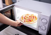 Katere hrane ne smemo pogrevati in zakaj? Close-up Of A Happy Woman Baking Pizza In Microwave Oven
