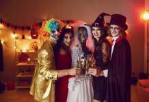 6 mitov o noči čarovnic Diverse group of happy young people drinking and having fun at Halloween party at home. Smiling adult multiethnic male and female friends in scary costumes standing together and clinking flute glasses
