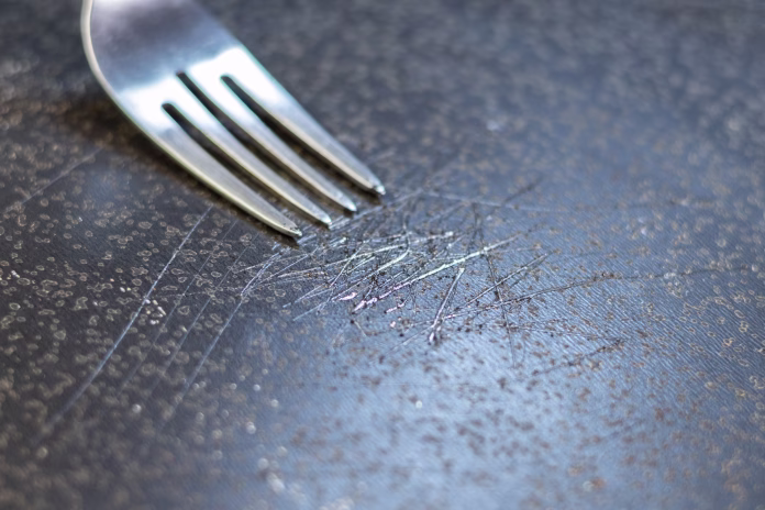 Fork in scratched non-stick coated pan. Dangerous chemicals in cookware.