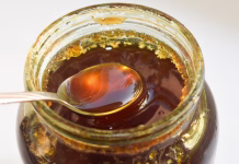 Ali med res pomaga pri spancu? Fresh honey is poured into a glass jar. close-up, selective focus and blurred background. Taking a spoon of honey from jar top view photo
