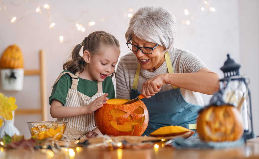 Happy family preparing for Halloween. Grandmother and granddaughter carving pumpkins at home.