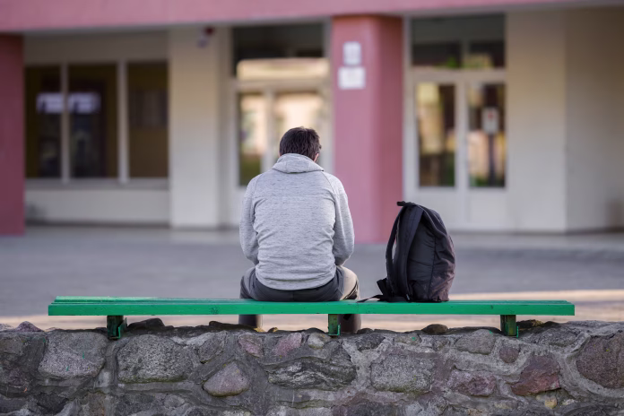 One young man sitting on bench at school yard. Break time. Back view.