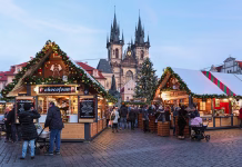 Najlepši božični sejmi v letu 2025 Prague, Czech Republic - December 11, 2019: Christmas market at Old Town Square with the city's main Christmas tree close to Jan Hus Monument in the evening. The Gothic church of Our Lady before Tyn is located in the background. Unknown people walk around the market stalls.