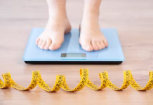 Znanstveniki odkrili naravno molekulo, ki zavre apetit Tape measure and woman feet standing on weigh scales.Diet, weight loss and feet of a woman on a scale for body check, measure and balance to lose weight on the floor. Obesity, scales and girl with tape