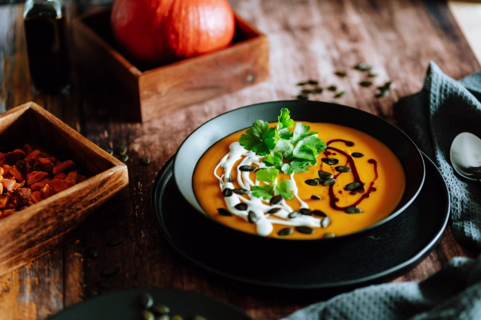 Vegetarian, homemade pumpkin cream soup in a bowl on wooden table.