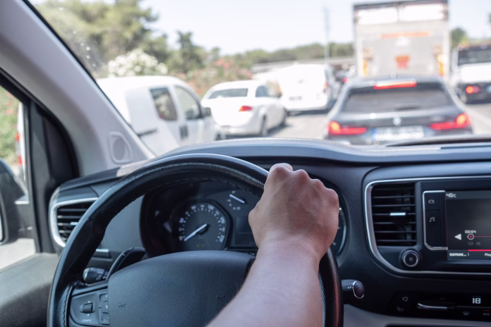 vehicles-are-lined-up-in-a-traffic-jam-on-a-busy-road-during-the-day-with-a-close-up-view-of-a-hand-gripping-the-steering-wheel-of-a-car-stockpack-istock Vehicles are lined up in a traffic jam on a busy road during the day, with a close-up view of a hand gripping the steering wheel of a car.