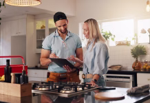 Če boste doma taki, boste učinkovitejši v življenju Woman, man and plumber with clipboard in home for invoice, report and talk for repair in kitchen. People, handyman and client with checklist for drainage system, inspection and smile at apartment
