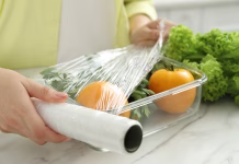 Ne uporabljajte plastične folije: TO so okolju prijaznejše alternative Woman putting plastic food wrap over glass container with fresh vegetables at white marble table, closeup