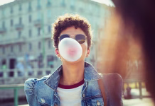 Sploh se ne zavedate tveganja! Zaradi tega boste prenehali žvečiti žvečilni gumi za vedno … Young african girl in sunglasses with curly hair puffs bubble of chewing gum in city street. Brazilian young woman inflates pink chewing gum. Stylish woman making bubblegum of chewing gum.