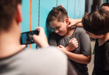 Novi zakon o kazenski obravnavi mladoletnikov: več individualnega pristopa in hitrejši postopki A young boy is being bullied by peers at school. The boy is upset as another boy grabs his neck. A third boy records the bullying incident on his phone. Bullying of teenager in high scool.