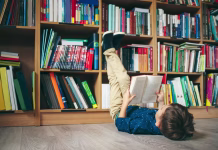 Katera država prebere največ knjig? Kam se uvršča Slovenija? Boy laying on the floor with the feet up, reading a book against multi colored bookshelf in library. Education, Knowledge, Bookstore, Lecture. Pupil holds a book in his hands.