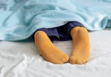 Spite v nogavicah? 4 nevarne stvari se lahko zgodijo vašim stopalom Child sleeps soundly under a blue blanket, an yellow sock peeking out, evoking a sense of peaceful rest
